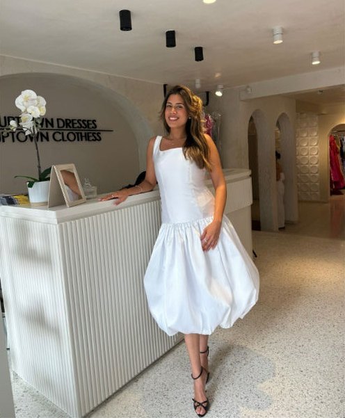 Mujer con un vestido blanco abullonado en la recepción del nuevo showroom, junto al letrero de Uptown Dresses