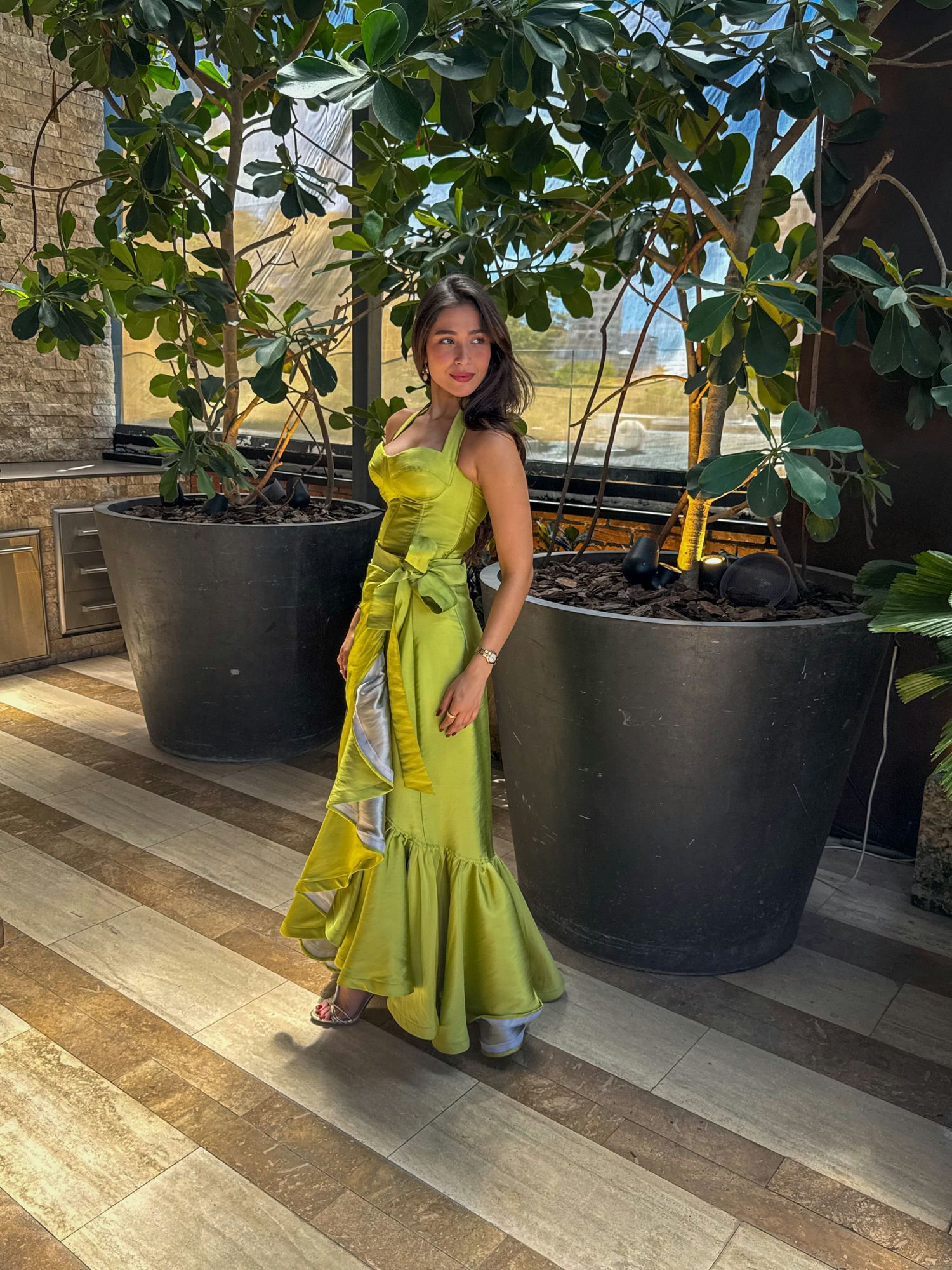 Mujer con un vestido mermaid verde limón de pie entre jardineras